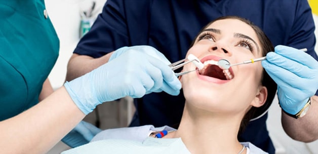 smiling woman head back in dentist chair, dentist inspecting her teeth