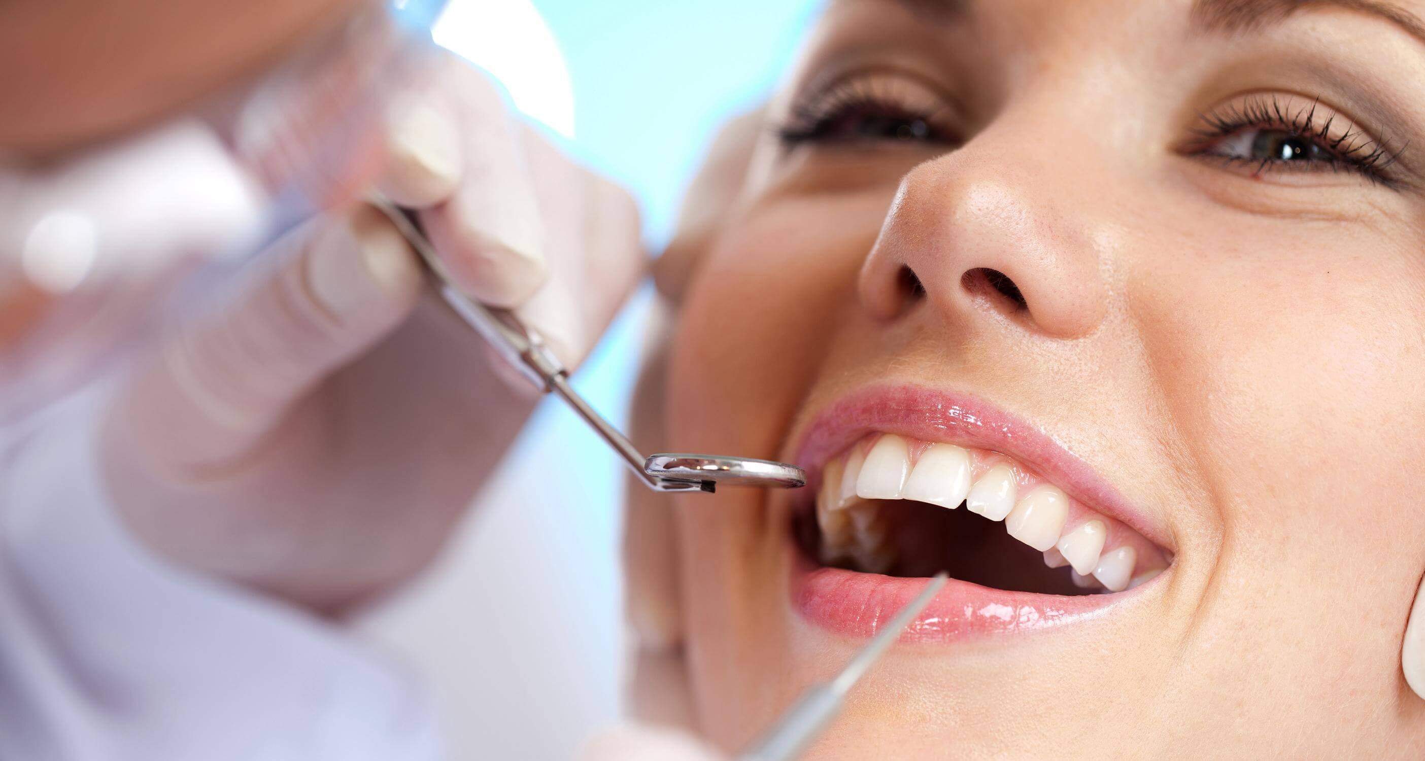 dentist inspecting a woman's teeth, woman smiling