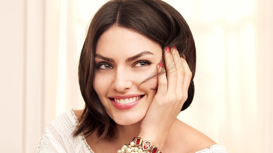 Brown haired Woman smiling, holding hair back from face
