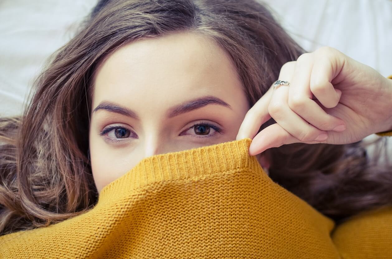 young woman covering lower half of face with orange sweater
