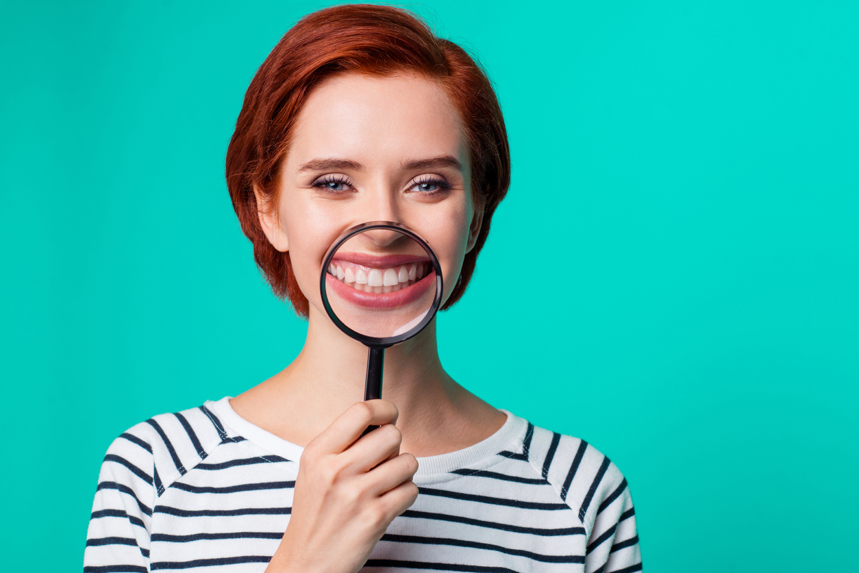 Smiling red-haired woman holds magnifying glass to teeth
